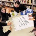 Students sit at a table in a library in Italy as one takes notes